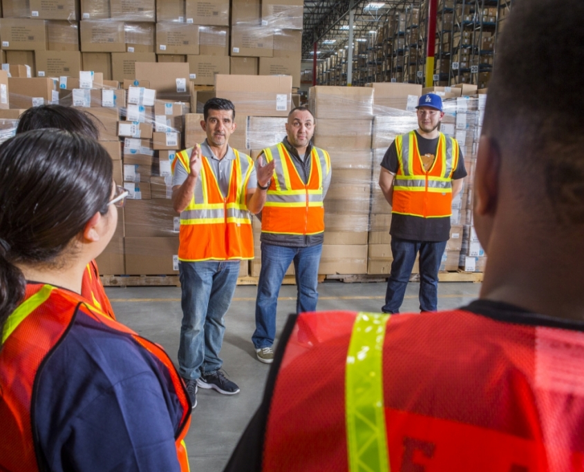 Warehouse manager with orange hi-vis vest leading team